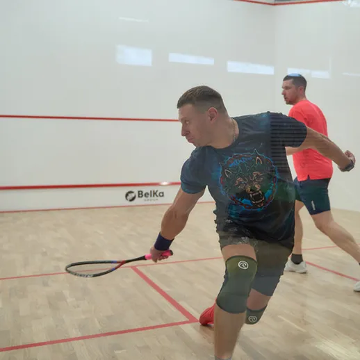 Игроки в сквош на корте во время турнира на спортивном стадионе в ярком освещении, сосредоточенные на игре