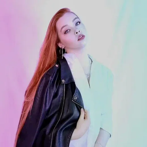 Модель с длинными рыжими волосами позирует в кожаной куртке на фоне разноцветного освещения