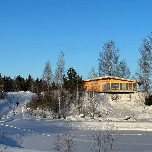 Зимний пейзаж с деревянным домом на фоне снежного леса и ясного неба