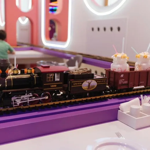 Маленький паровозик с напитками проезжает мимо столов в красочном кафе