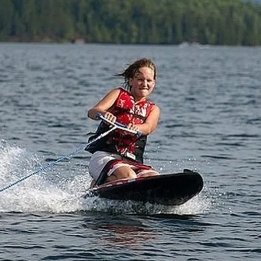 Женщина, занимающаяся водными лыжами на озере среди зелёных деревьев в солнечный день