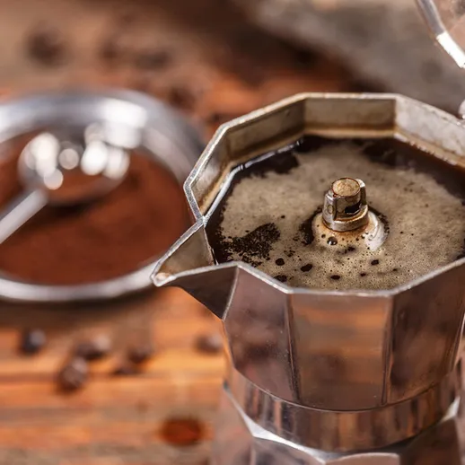 Приготовление кофе в итальянской кофеварке на деревянном столе с кофейными зернами вокруг