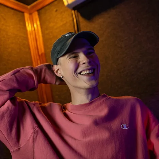 Молодой человек в розовом свитере улыбается во время записи музыки в студии в вечернее время