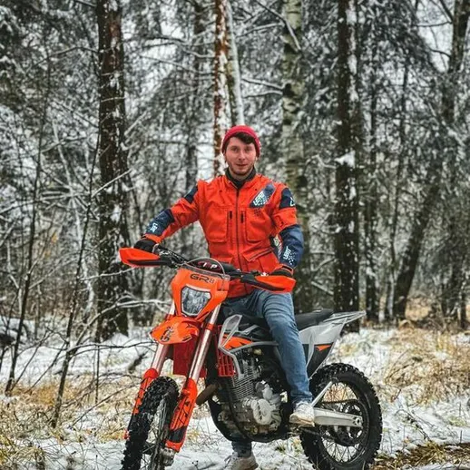 Молодой человек ездит на мотоцикле по снежному лесу в зимний день