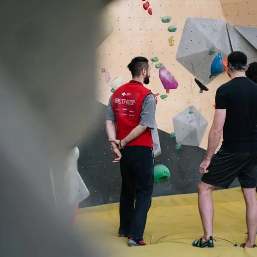 Тренировка скалолазов в спортзале: инструктор показывает технику на стенде