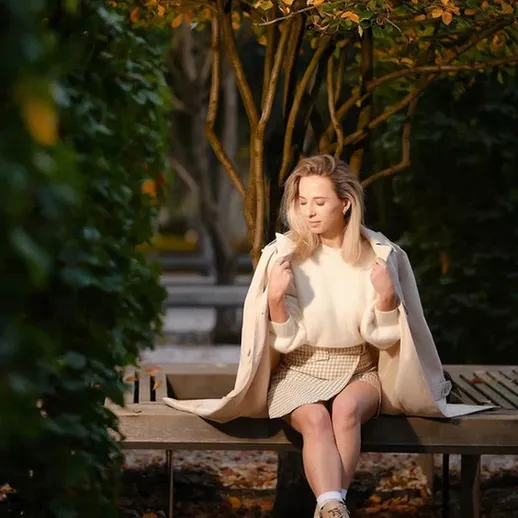 Осенний день в парке: девушка в свете тёплого солнечного света сидит на скамейке в окружении деревьев