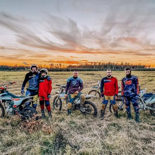 Группа мотоциклистов на фоне заката в поле у леса, наслаждающихся активным отдыхом на внедорожниках