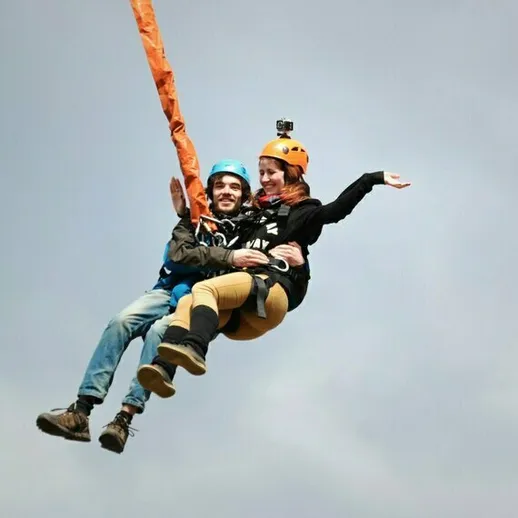 Два человека наслаждаются полетом на тарзанке над красивыми пейзажами в ясный день