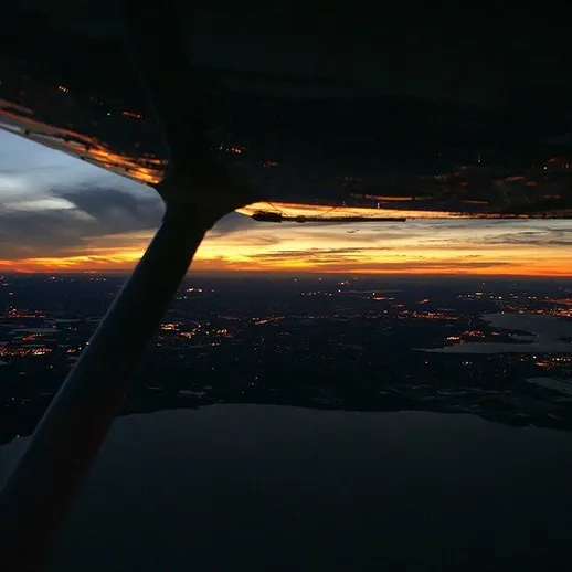 Закат над городом, вид из окна малой авиации, вечер, спокойные воды и огни города