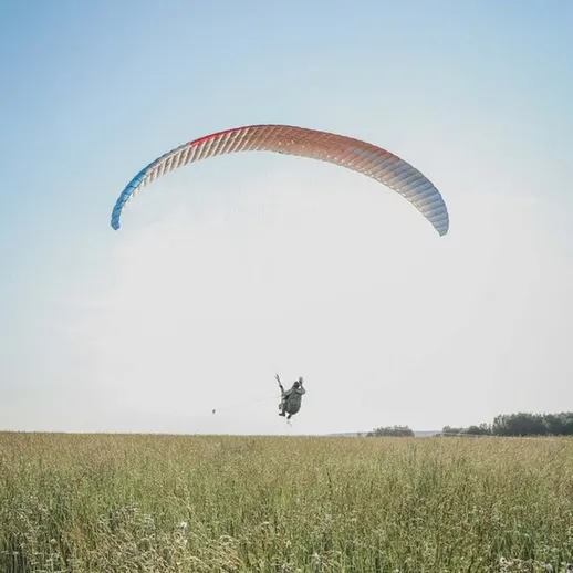 Параглайдер в небе над зелёным полем в ясный день, демонстрирующий захватывающие моменты свободного полёта