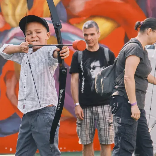 Мальчик стреляет из лука на празднике в парке с яркой стеной изображений