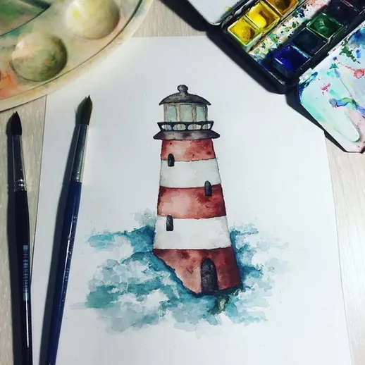 Акварельный рисунок маяка с красными и белыми полосами, окруженного морскими волнами, с кистями и краской на столе