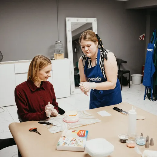 Урок по декорированию тортов в уютной студии, где учитель показывает ученице техники украшения