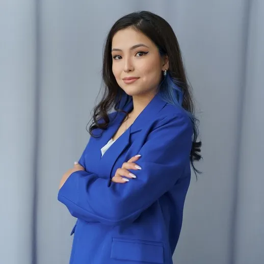 Женщина в синем костюме позирует с уверенностью на фоне нейтральных стен