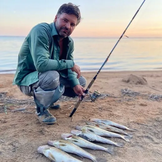 Рыбак на берегу озера с уловом на фоне заката в спокойной обстановке