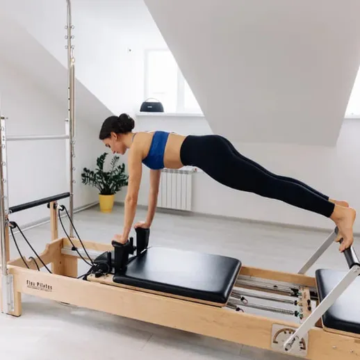 Женщина выполняет упражнение на реформере пилатеса в светлом помещении спортивного зала