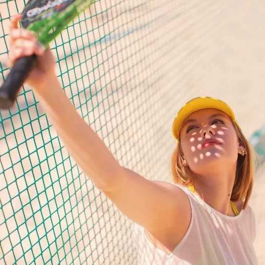 Женщина играет в теннис на песчаном корте в солнечный день, маленький теннисный мячик в руке