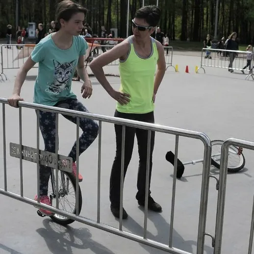 Две девушки учатся кататься на моноцикле в парке среди деревьев в солнечный день