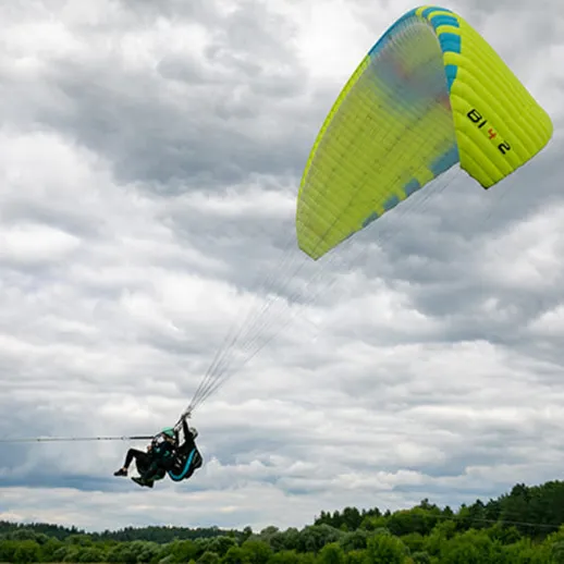 Парапланерист летит над зелеными холмами в облачном небе весной