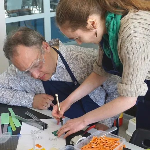 Мужчина и женщина занимаются рукоделием в учебном центре, создавая уникальные поделки с использованием бумаги и цветных материалов