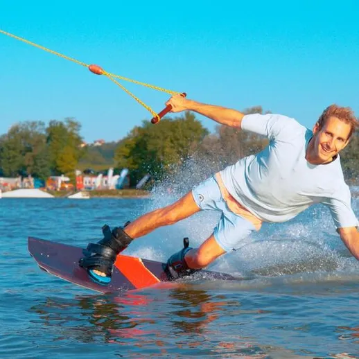 Мужчина катается на вейкборде на озере в солнечный день с друзьями на берегу