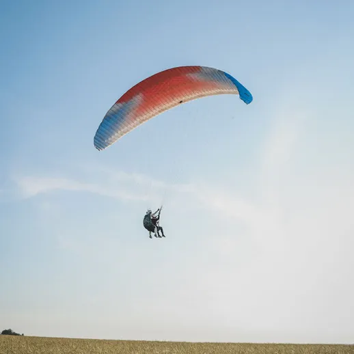 Парапланерист над зелеными полями под голубым небом в ясный день