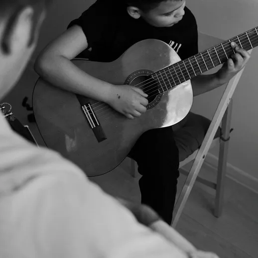 Мальчик играет на гитаре, обучаясь музыке в уютной комнате