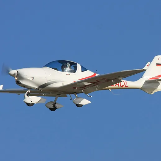 Летающий самолет над ясным голубым небом, выполненный в белом цвете, с пилотом на борту, днем