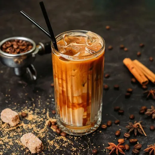 Освежающий кофе со льдом в стеклянном стакане на столе с корицей и кофе в зернах