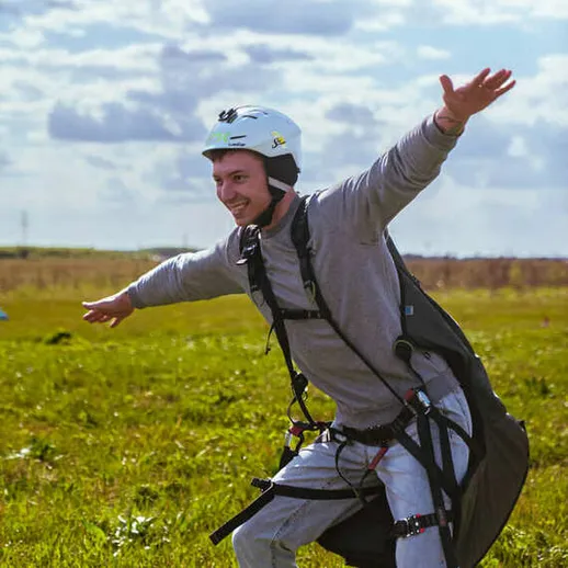 Парашютист готовится к прыжку с парашютом на зеленом поле под ясным небом в солнечный день