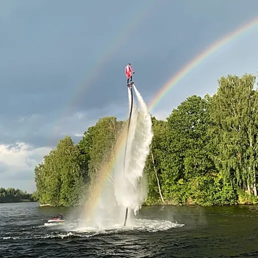 Катающийся на флайборде человек под радугой на озере в ясный день