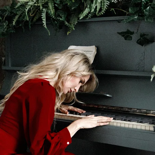Женщина в красном платье играет на пианино в окружении зелени