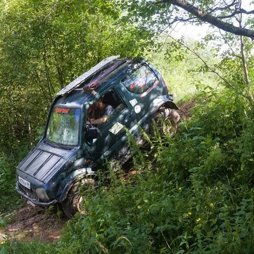 Автомобиль застрял на лесной тропе, окруженный зелеными деревьями и кустами, в летний день