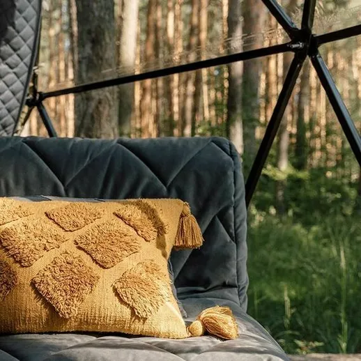 Уютная зона отдыха в лесу с серым диваном и желтой подушкой на фоне сосен в солнечный день