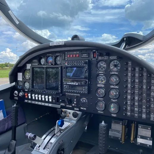 Кабина управления легкомоторного самолета с множеством приборов и облачным небом за окном