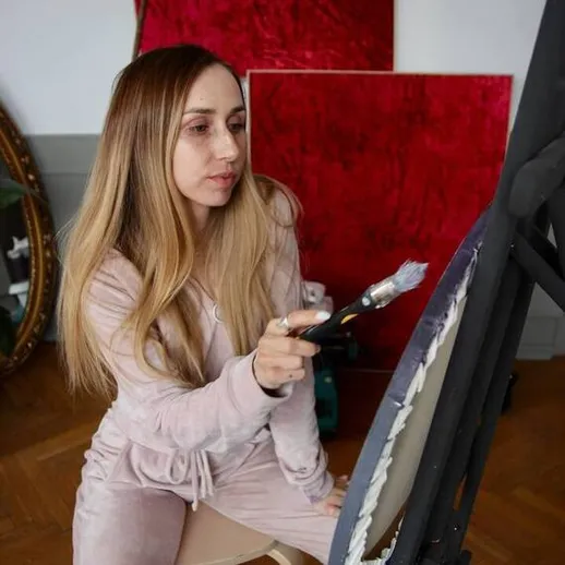 Молодая женщина рисует картину в уютной студии с красными фонами и зеркалом