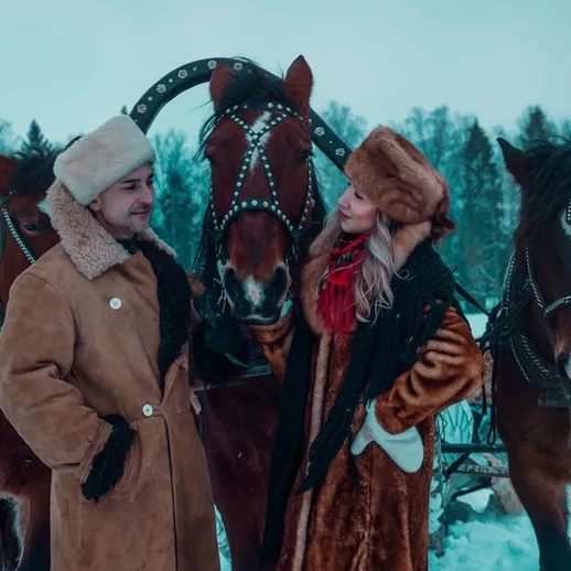 Пара в зимней одежде на фоне лошадей в снегу в морозное утро в лесу России