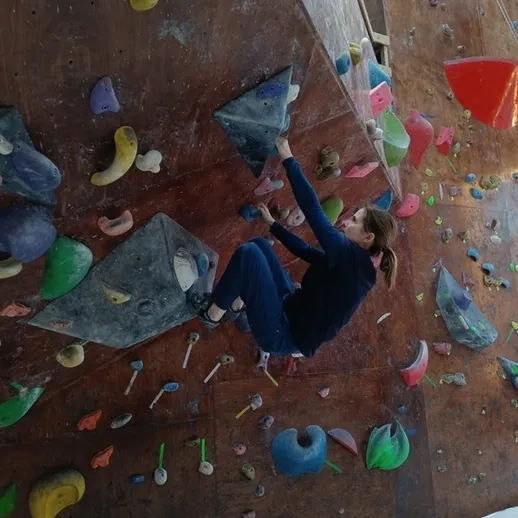 Девушка занимается скалолазанием в закрытом зале на разноцветных зацепках в поздний вечер