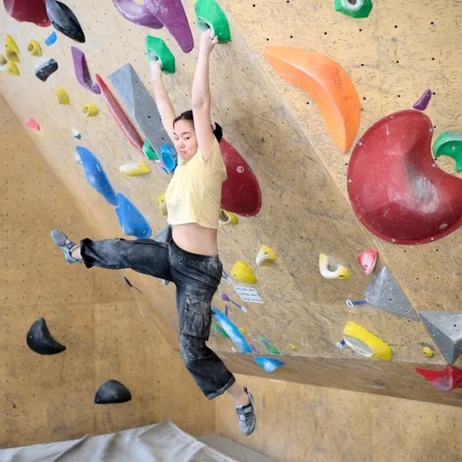 Спортсменка преодолевает скалодром в зале для боулдеринга в Москве под яркими цветными зацепами