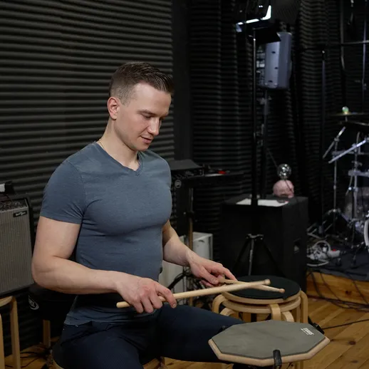 Музыкант играет на барабанах в репетиционной студии в вечернее время, сосредоточенно тренируясь на ритме