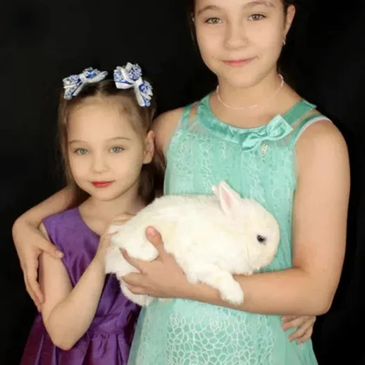 Две девочки держат белого кролика на черном фоне в уютной обстановке