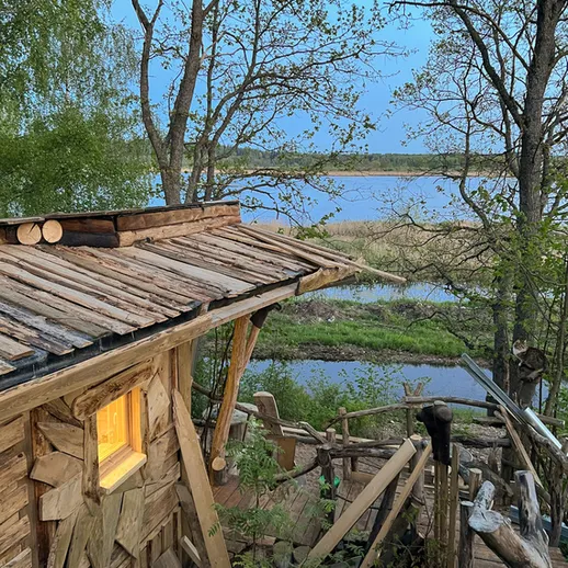 Уютная деревянная хижина на берегу реки, окруженная зелеными деревьями, в вечернее время на фоне заката