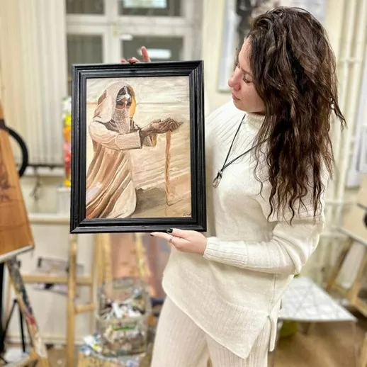 Молодая художница показывает свою работу в арт-студии, освещённой естественным светом, в уютной атмосфере