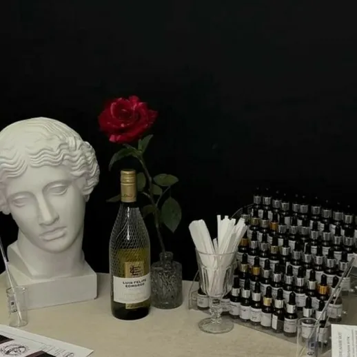 На столе расположены головка статуи, бутылка вина и красная роза на черном фоне
