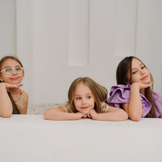 Три девочки позируют с улыбками в светлом помещении на фоне нейтральной стены