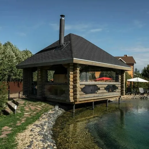 Красивая деревянная беседка на берегу озера с зелеными насаждениями и спокойной водой в солнечный день