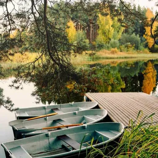 Лодки на берегу тихого озера в лесу осенью, окруженные яркими деревьями и спокойной водой