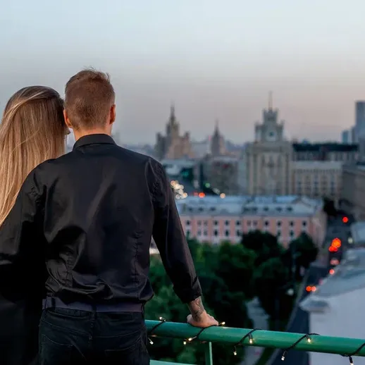 Пара наслаждается закатом над Москвой с высоты здания, смотря на величественные городские пейзажи и огни