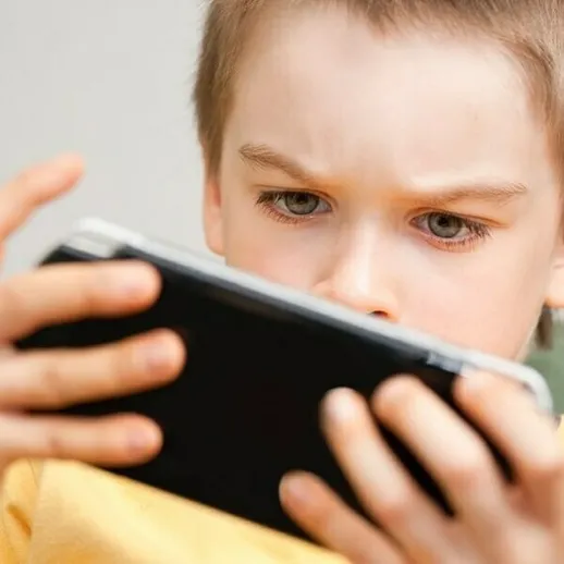 Мальчик играет на смартфоне, сосредоточенно смотря на экран, сидя на диване в уютной комнате