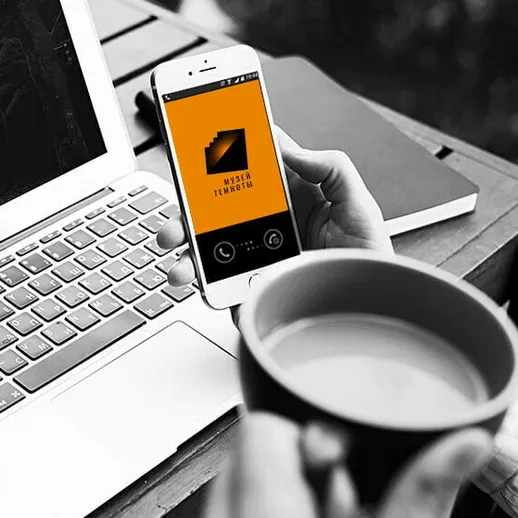 Работающий человек с телефоном и чашкой кофе на фоне ноутбука в уютном офисе